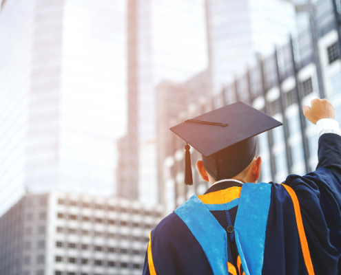 Man in graduation cap raises fist toward tall buildings