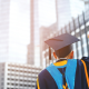 Man in graduation cap raises fist toward tall buildings