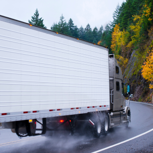 Semi truck driving on a wet road carrying a refrigerated trailer.