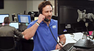 Man in blue polo talks on a black chorded phone