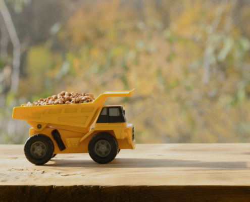 Yellow toy dump truck filled with pebbles on a wooden table
