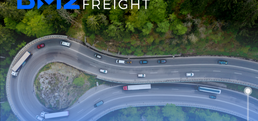 Aerial view of a wooded highway with semi trucks and cars driving around a road that circles through the woods.