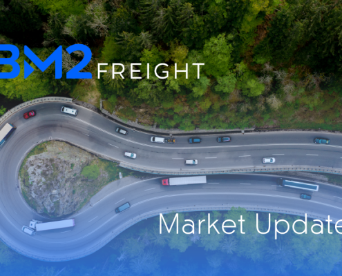 Highway centered between dense trees with cars and semi trucks driving on it and text that reads "Market Update' in the bottom right corner, and a BM2 Freight logo in the upper left corner.